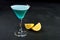 Blue cold cocktail in martini glass with lemon dark background