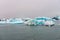 Blue colored melting icebergs floating around in Jokulsarlon glacier lagoon in Iceland during foggy weather.