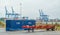 Blue container, red semitrailer and cranes in a port terminal