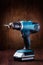 Blue cordless screwdriver with a drill on wooden table with wooden background