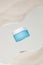 A blue cosmetic jar with a white lid is displayed on an acrylic sheet on a beige sand background. Vibrant summer mood for