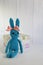 A blue crocheted banny rabbit sits near a gift box on a white background