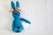 A blue crocheted banny rabbit takes a white heart and sits on a white background