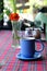 Blue cup of coffee on quilt table cloth with vase of orangy red spring flower on the background