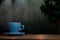 A blue cup of coffee resting on a wooden cafe table against a backdrop of ambient lighting.