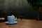 A blue cup of coffee resting on a wooden cafe table against a backdrop of ambient lighting.