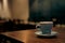 A blue cup of coffee resting on a wooden cafe table against a backdrop of ambient lighting.