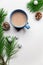 Blue cup of hot cacao or cappuccino with cinnamon standing on white table with pine branches and silver bulbs. Merry Christmas