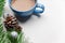 Blue cup of hot cacao or cappuccino with cinnamon standing on white table with pine branches and silver bulbs. Merry Christmas