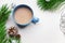 Blue cup of hot cacao or cappuccino with cinnamon standing on white table with pine branches and silver bulbs. Merry Christmas