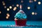 A blue cupcake with a glowing candle and bold red sprinkles