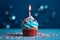 A blue cupcake with a glowing candle and bold red sprinkles