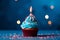 Blue cupcake, red sprinkles, and a lit candle on blue backdrop