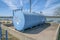 Blue cylindrical propane gas tank against Lake Austin and cloudy blue sky