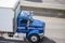 Blue day cab middle class rig semi truck with box trailer driving on the highway road for timely delivery