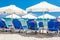 Blue deckchairs, white sun umbrellas parasols, resting tourists on the beaches of Greek Paralia resort city with warm Aegean sea