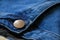 Blue denim jean metal button rivet with seam texture and background.