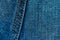 Blue denim jeans background with seam and orange thread stitches. Casual urban classic fashion tailoring clothing concept