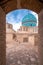 Blue dome of Vali Shrine mosque viewed through a rooftop stone arch. On the rooftop of Shah Nematollah Vali Shrine, Mahan, Iran