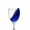 A blue drink is poured into wine glass causing a splash, isolated on white background