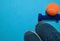 Blue dumbbell, sneakers and orange tennis ball indicating workout plan on blue background.