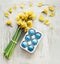 Blue Easter egg in holder with yellow daffodils flowers bunch on white shabby chick background. Top view