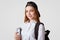 Blue eyed delighted schoolgirl holds book, carries backpack, wears black cap, going to library, reads and cramms material for exam