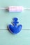 Blue felt anchor ornament and white thread on wooden background. Embroidery crafts for kid. Step. Closeup. Top view