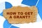 On the blue financial charts is a piece of cardboard that says - How To Get A Grant