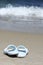 Blue flip flops on sand beach in front of sea wave