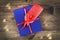 Blue gift box with red ribbon, blank gift tag and bokeh on wooden background.