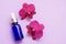 Blue glass bottle filled by essence or serum with orchid extract on purple background with bright blossoming orchids phalaenopsis.