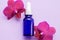 Blue glass bottle filled by essence or serum with orchid extract on purple background with bright blossoming orchids phalaenopsis