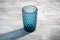 Blue glass geometric cup with colorful shadow light rays on stone concrete background