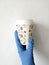 A blue-gloved hand holds a paper Cup of coffee on a white background.