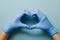 Blue gloved hands in heart shape on light blue background, showcasing precision and care