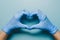 Blue gloved hands in heart shape on light blue background, showcasing precision and care