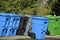 Blue gree black and gray trash cans on street or road trash day while sanitation workers collect garbage and recycling