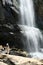 Blue haired girl in a hat staying under Ramboda waterfall in Sri Lanka. Watching water flowing at a popular touristic viewpoint in