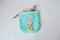 Blue handmade zipper pouch with cute doll, hair pins, mascara and hair tweezers over white