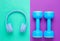 Blue headphones, plastic dumbbells on mint purple background. Sports with music. Flat lay.