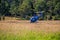 Blue helicopter is low flying over the land. Agricultural work. Transportation aircraft. Spraying fields