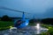 A blue helicopter is parked on a private helipad against a blue evening.