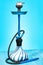 Blue hookah with black rubber tube and blue and white flask on light blue background.