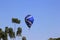 Blue hot air balloon rising next to trees. Blue clear sky.