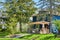 Blue house surrounded by green summer trees, landscaping, brick and pillar porch patio