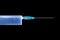 Blue illuminated syringe with sharp needle close up on black iso