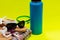 Blue Insulated Stainless Steel Bottle, Beach Towel, Flip Flops, Blue Rim Glass with Water and Black Sunglasses on yellow