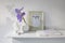 Blue iris in a corrugated vase with piece of craft paper on a white table. Figurine of the angel. Frame with sign Enjoy. Place