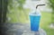 Blue italian soda in takeaway cup on marble stone table with blurred green grass and bamboo in background,selective focus